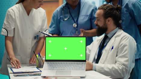 Team-of-doctors-consulting-analytics-next-to-green-screen-on-laptop