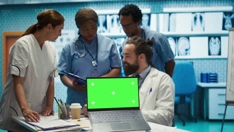 Team-of-doctors-consulting-analytics-next-to-green-screen-on-laptop-in-cabinet