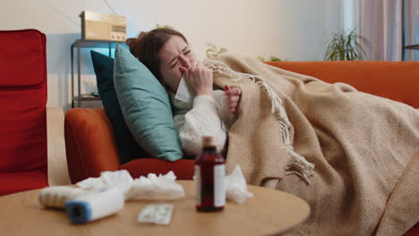 Sick-ill-woman-suffering-from-cold-or-allergy-sitting-on-home-sofa-sneezes-wipes-snot-into-napkin