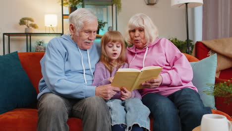 Kind,-Mädchen,-Enkelin-Mit-Großeltern-Lesen-Interessantes-Buch-Zusammen-Sitzen-Auf-Der-Couch-Zu-Hause