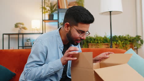 Dissatisfied-Indian-man-customer-open-cardboard-box-receive-damaged-broken-wireless-headphones