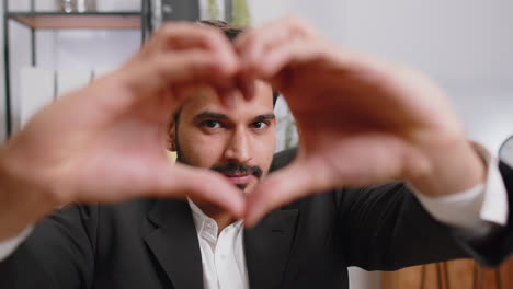 Indian-business-man-makes-symbol-of-love,-showing-heart-sign-to-camera,-express-romantic-feelings