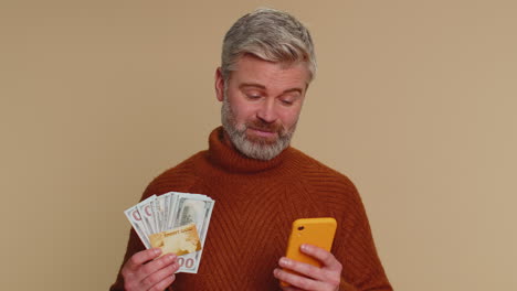 Senior-man-using-credit-bank-card-and-smartphone-while-transferring-money-purchases-online-shopping