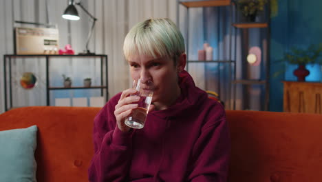 Thirsty-young-woman-sitting-at-home-holding-glass-of-natural-aqua-make-sips-drinking-still-water