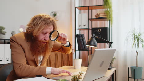 Business-man-working-at-home-office-holding-magnifying-glass-looking-at-laptop-screen-wow-expression