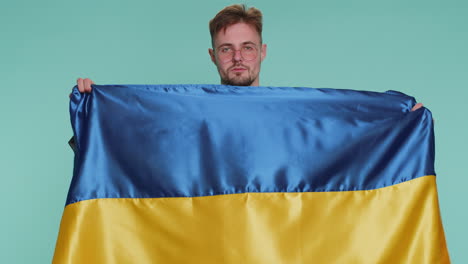 Man-holding-Ukraine-national-flag,-showing-victory-sign-against-war,-hoping-for-success-and-win