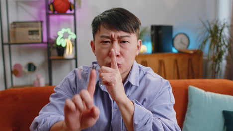 Asian-man-presses-finger-to-lips-makes-silence-hush-sign-do-not-tells-gossip-secret,-quiet-at-home