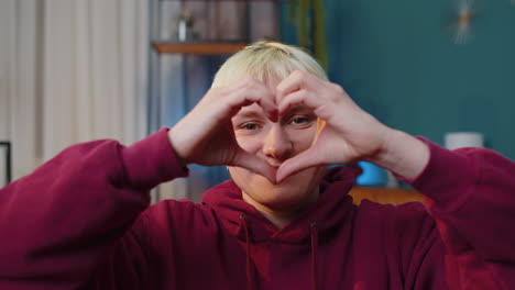 Happy-blonde-young-woman-makes-symbol-of-love-showing-heart-sign-to-camera-express-romantic-feelings