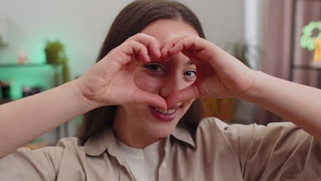 Una-Joven-Feliz-Hace-Un-Símbolo-De-Amor-Mostrando-Un-Signo-De-Corazón-A-La-Cámara-Expresa-Sentimientos-Románticos