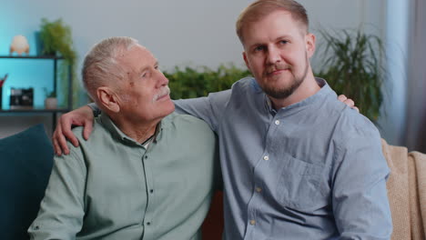 Portrait-of-senior-grandfather-with-young-adult-man-grandson-smiling-happy-embracing-hugging-at-home