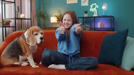 Child-girl-looking-approvingly-at-camera-showing-thumbs-up-like-sign-positive-with-cute-beagle-dog