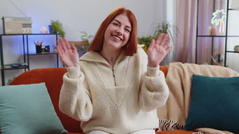 Pretty-woman-smiling-friendly-at-camera,-waving-hands-gesturing-hello,-hi,-greeting-at-home-on-sofa