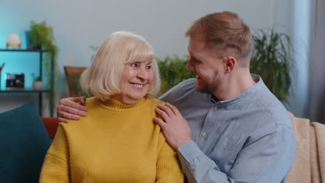 Portrait-of-senior-grandmother-with-young-adult-man-grandson-smiling-happy-embracing-hugging-at-home