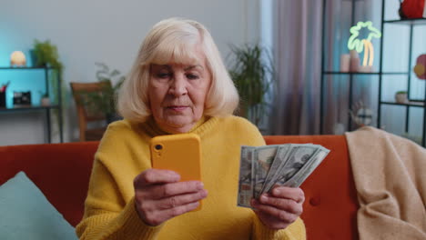 Mujer-Abuela-Feliz-Contando-Dinero-En-Efectivo-Usando-Un-Teléfono-Inteligente,-Ingresos-Ahorra-Lotería-Ganar-Presupuesto-En-Casa