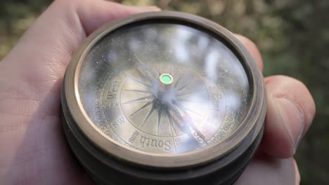 Traveler-hand-holds-a-old-directional-compass-in-summer-forest.-Person-use-compass-to-find-location.-Travel-concept-close-up.