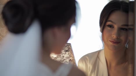 Bride-in-white-boudoir-dress-stay-near-mirror,-looking-at-reflection,-wedding-preparations-at-home