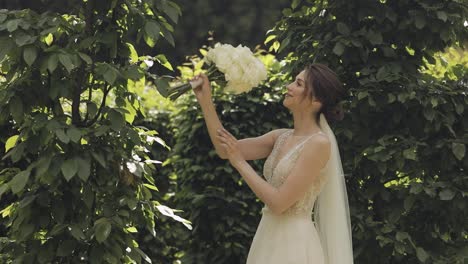 Beautiful-stylish-bride-in-white-wedding-dress-and-veil-holding-wedding-bouquet-in-hands-in-park