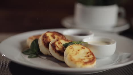 Chef-Espolvoreando-Azúcar-En-Polvo-Sobre-Deliciosos-Panqueques-De-Durazno-Con-Requesón-En-Un-Plato-Sobre-La-Mesa