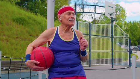 Senior-man-grandfather-after-sport-basketball-training-sitting,-listening-music-on-playground-court