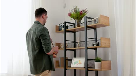 Happy-Arranging-Decor-on-Shelf-at-Home.home-improvement-and-decoration-and-people-concept--happy-smiling-man-arranging-decor-on-shelf