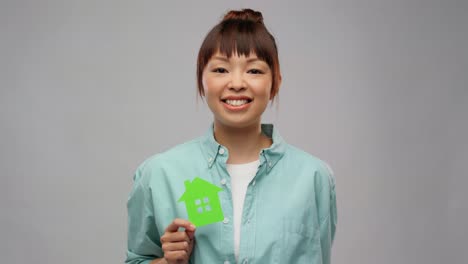 Asian-Woman-with-Green-House-Showing-Thumbs-Up.eco-living,-environment-and-sustainability-concept--portrait-of-happy-smiling-young-asian-woman-in-turquoise-shirt-holding-green-house-and-showing-thumbs-up-over-grey-background