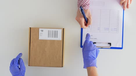 Hands-Giving-Parcel-Box-to-Customer-Signing-Papers.health-protection,-safety-and-pandemic-concept--hands-of-delivery-woman-in-gloves-with-clipboard-giving-parcel-box-to-customer-signing-papers