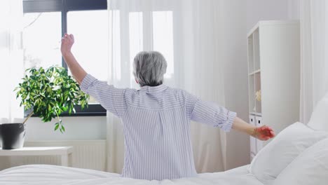 Senior-Woman-Stretching-on-Bed-at-Home-Bedroom.old-age-and-people-concept--senior-woman-in-pajamas-sitting-and-stretching-on-bed-at-home-bedroom