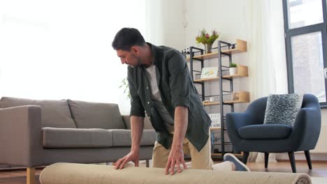 Happy-Smiling-Young-Man-Unfolding-Carpet-at-Home.household,-home-improvement-and-interior-concept--happy-smiling-young-man-unfolding-carpet