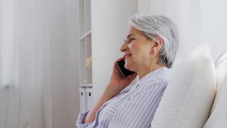 Senior-Woman-Calling-on-Smartphone-in-Bed-at-Home.old-age,-technology-and-people-concept--happy-smiling-senior-woman-in-pajamas-calling-on-smartphone-sitting-in-bed-at-home-bedroom