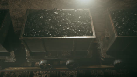 Old-mine-wagons-full-of-coal-moving-slowly-through-the-narrow-passage.-Seamless-looping-top-view-of-an-endless-row-of-coal-trolleys-in-a-dark-underground-tunnel.-Bright-light-at-the-end-of-tunnel.