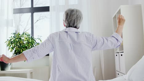 Senior-Woman-Stretching-on-Bed-at-Home-Bedroom.old-age-and-people-concept--senior-woman-in-pajamas-sitting-and-stretching-on-bed-at-home-bedroom