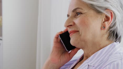 Senior-Woman-Calling-on-Smartphone-in-Bed-at-Home.old-age,-technology-and-people-concept--happy-smiling-senior-woman-in-pajamas-calling-on-smartphone-sitting-in-bed-at-home-bedroom