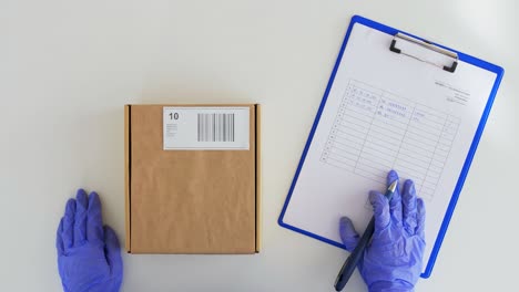 Hands-in-Gloves-with-Parcel-Box-and-Clipboard.health-protection,-safety-and-pandemic-concept--hands-of-delivery-woman-in-gloves-with-clipboard-giving-parcel-box-to-customer