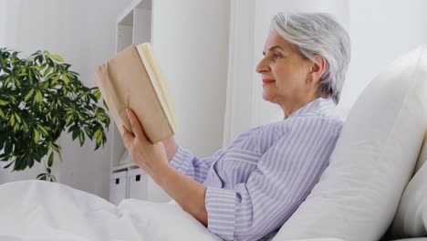 Mujer-Mayor-Leyendo-Un-Libro-En-La-Cama-En-El-Dormitorio-De-Su-Casa.-Tecnología,-Concepto-De-Vejez-Y-Personas.-Mujer-Mayor-Leyendo-Un-Libro-En-La-Cama-En-El-Dormitorio-De-Su-Casa.