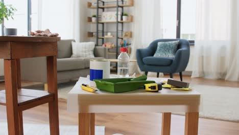 Woman-Taking-Break-While-Renovating-Table-at-Home.repair,-diy-and-home-improvement-concept--woman-taking-protective-gloves-off-and-leaving-room-with-old-table-and-tools