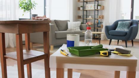 Woman-Taking-Break-While-Renovating-Table-at-Home.repair,-diy-and-home-improvement-concept--woman-taking-protective-gloves-off-and-leaving-room-with-old-table-and-tools