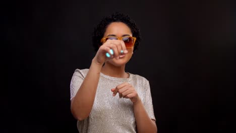 Woman-in-Sunglasses-Dancing-with-Glowing-Lines.leisure-and-people-concept--happy-african-american-woman-in-sunglasses-dancing-over-black-background-with-animated-glowing-neon-lines