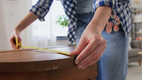 Woman-with-Ruler-Measuring-Table-for-Renovation.repair,-diy-and-home-improvement-concept--woman-with-ruler-measuring-old-round-wooden-table-for-renovation-and-writing-to-notebook