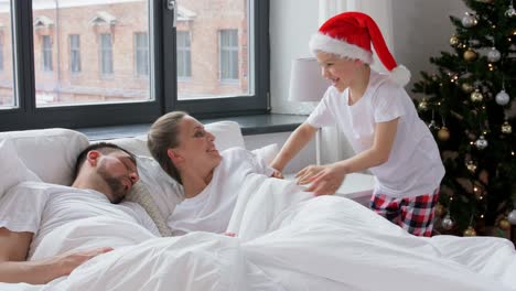 Glücklicher-Junge-Weckt-Seine-Eltern-Am-Weihnachtsmorgen.Familie,-Winterferien-Und-Menschenkonzept-Glücklicher-Kleiner-Sohn-Weckt-Seine-Mutter-Und-Seinen-Vater-Am-Weihnachtsmorgen