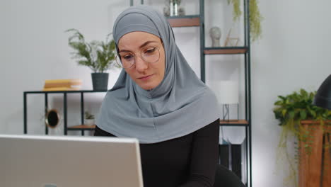 Muslim-business-woman-in-hijab-looking-at-camera-after-finishing-laptop-computer-work-at-home-office