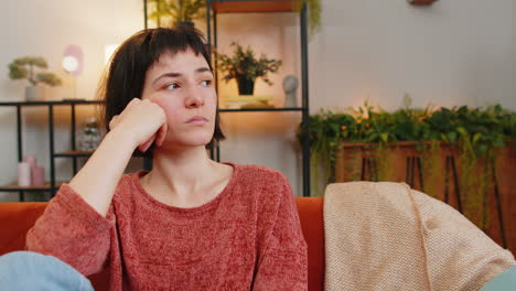 Sad-lonely-upset-Caucasian-young-woman-looks-pensive-depressed-feeling-bad-annoyed-at-home-room-sofa