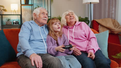 Child-girl-granddaughter-grandparents-using-joystick-controller-playing-console-videogame-at-home