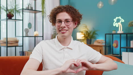 Smiling-man-at-home-makes-symbol-of-love-showing-heart-sign-to-camera-express-romantic-feelings