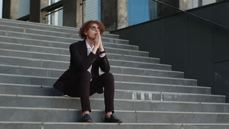 Nervous-businessman-manager-with-hands-joined-making-company-decision-pray-sitting-on-office-steps