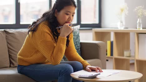 Asian-Woman-with-Papers-and-Calculator-at-Home.accounting,-taxes-and-finances-concept-young-asian-woman-with-papers-and-calculator-at-home