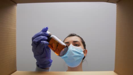 Mujer-Con-Mascarilla-Abriendo-Caja-De-Paquete-Con-Ropa.-Entrega-A-Domicilio,-Envío-Y-Concepto-De-Pandemia.-Mujer-Con-Mascarilla-Médica-Protectora-Y-Guantes-Abriendo-Caja-De-Paquete,-Mirando-Dentro-Y-Sacando-Ropa.