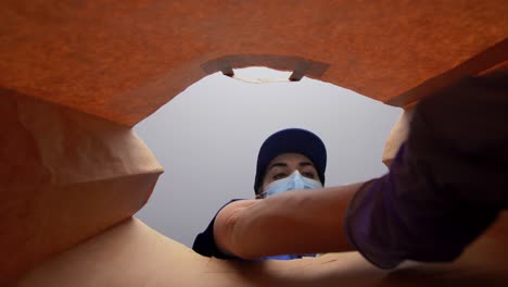 Woman-in-Gloves-and-Mask-Packing-Food-in-Paper-Bag.health-protection,-delivery-and-pandemic-concept-woman-in-protective-medical-gloves-and-mask-packing-chinese-takeaway-food-into-paper-bag