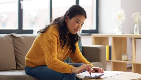 Asian-Woman-with-Papers-and-Calculator-at-Home.accounting,-taxes-and-finances-concept-young-asian-woman-with-papers-and-calculator-at-home