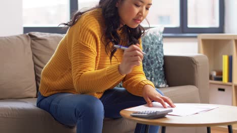 Asian-Woman-with-Papers-and-Calculator-at-Home.accounting,-taxes-and-finances-concept-young-asian-woman-with-papers-and-calculator-at-home