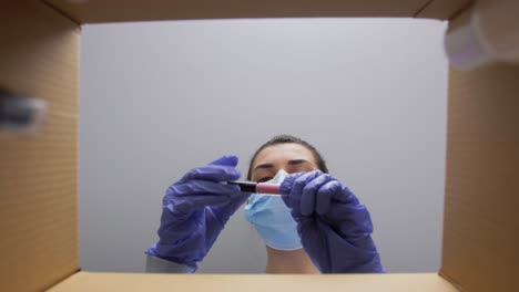 Mujer-Con-Mascarilla-Médica-Protectora-Y-Guantes-Desempacando-Una-Caja-De-Paquete-Con-Cosméticos.-Entrega-A-Domicilio,-Envío-Y-Concepto-De-Pandemia.-Mujer-Con-Mascarilla-Médica-Protectora-Y-Guantes-Desempacando-Una-Caja-De-Paquete-Con-Cosméticos-Y-Productos-De-Belleza.